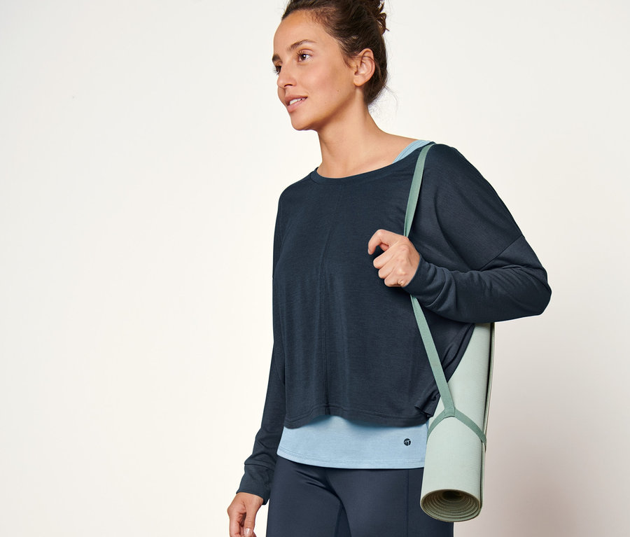 Frau trägt blaues 2-in-1-Sportshirt und Yogamatte.