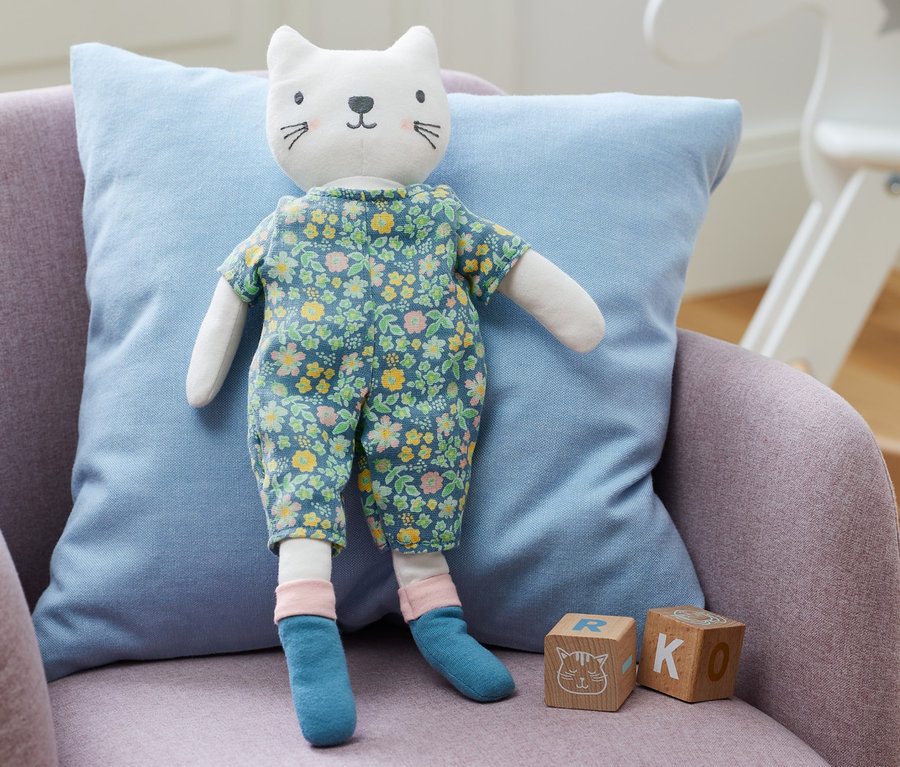 Eine Stoffpuppe »Kätzchen« steht auf einem lila Sessel mit einem blauen Kissen.
