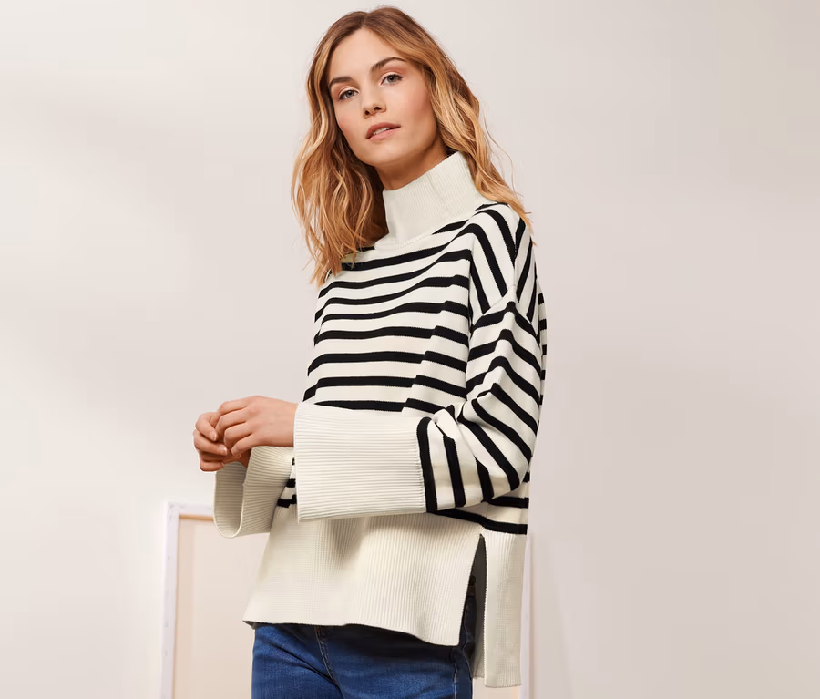 Frau posiert in einem Strickpullover mit Wolle, blauen Jeans und schwarzen Stiefeln.