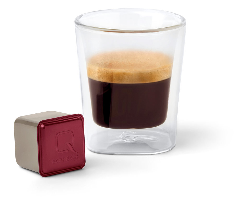 Eine Qbo Espresso APANECA ANA Kapsel steht neben einem Glas Espresso.