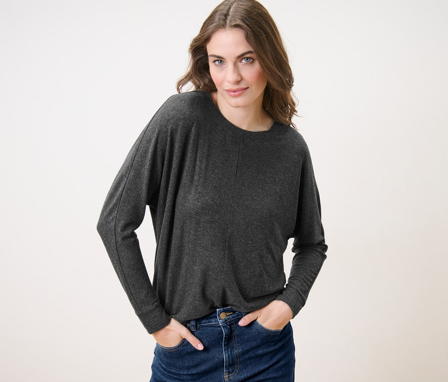 Frau posiert in Fledermausshirt und Jeans.