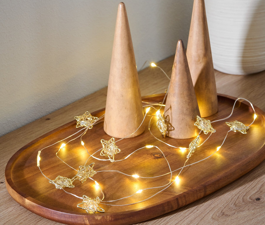 Auf einem Holztablett liegen drei Holzkegel und eine LED-Lichterkette in Sternform.