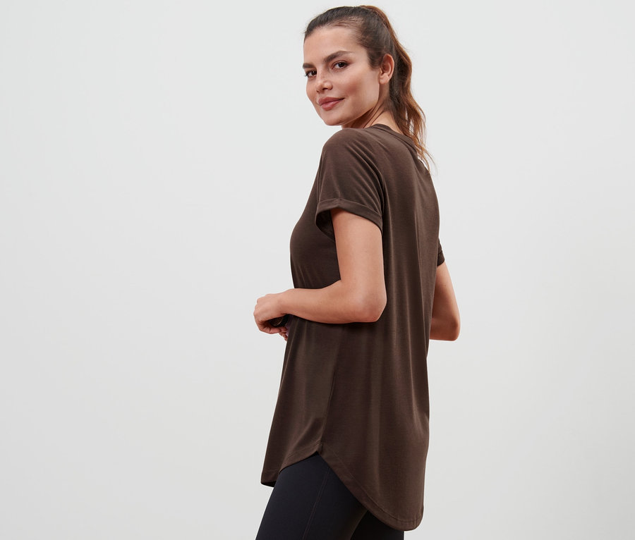 Eine Frau blickt über ihre Schulter und trägt ein braunes Longshirt.