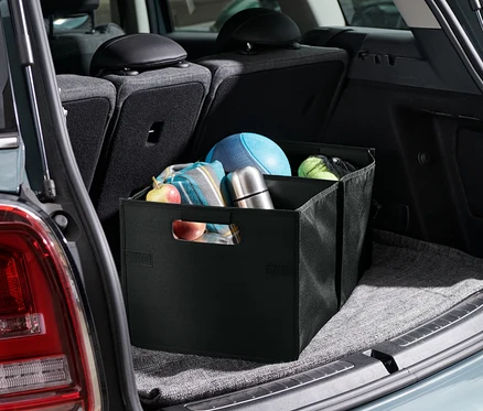 Eine Auto-Faltbox befindet sich im Kofferraum eines Autos. Im Inneren der Box befinden sich Obst, eine Decke, eine Thermoskanne und Bälle.