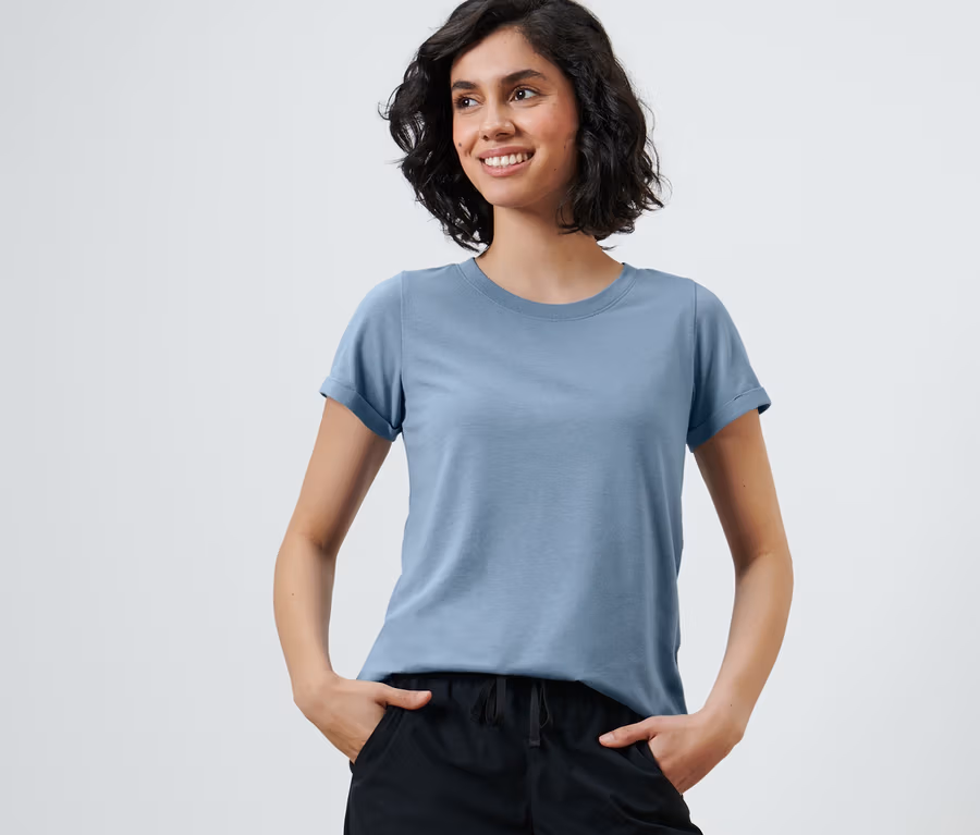 Lächelnde Frau mit Händen in den Taschen schwarzer Hosen und einem Funktionsshirt.