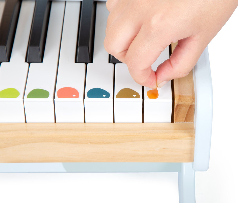 Eine Hand klebt einen orangefarbenen Aufkleber auf eine weiße Taste des small foot Klaviers »Groovy Beats«.