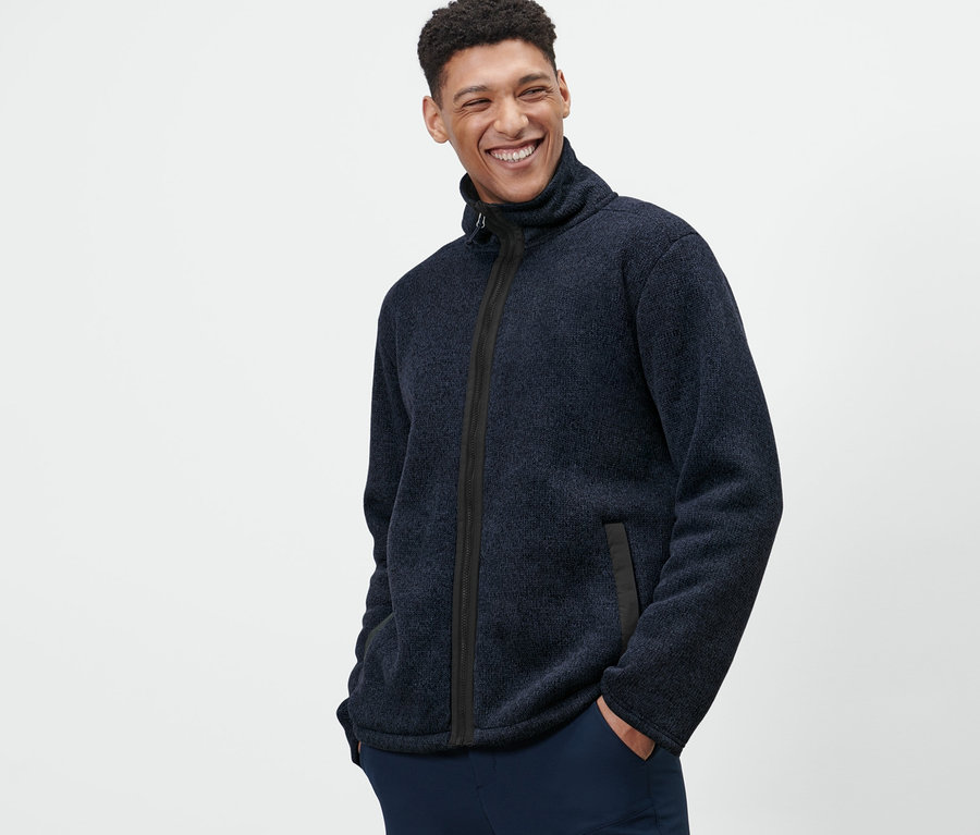 Mann posiert mit Händen in den Taschen in Strickfleece-Jacke.