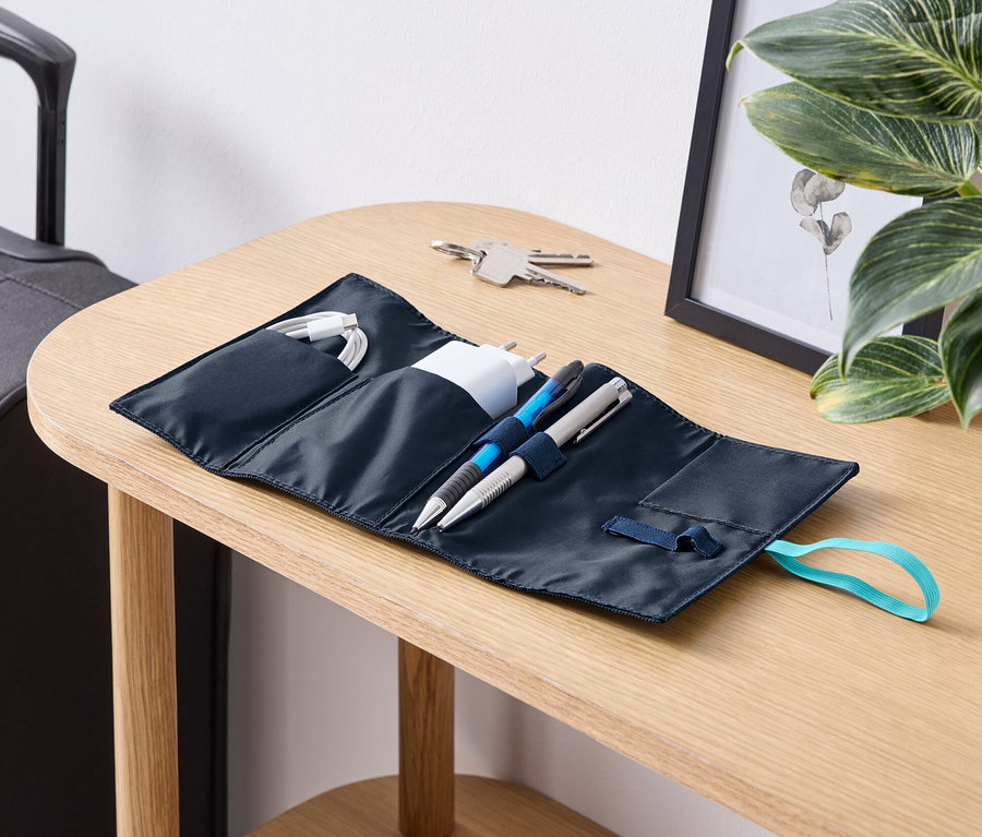 Auf einem Tisch liegt ein geöffneter Reise-Kabel-Organizer mit Kabeln, Ladegerät und Stiften.