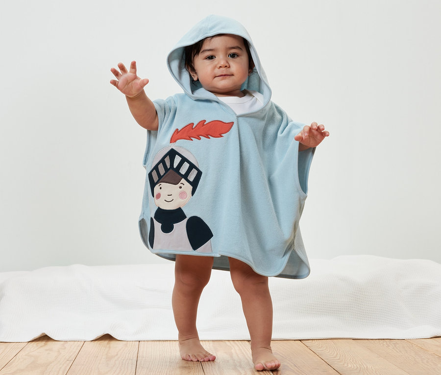 Ein Kind posiert in einem hellblauen Frottierponcho, Ritter mit Kapuze.