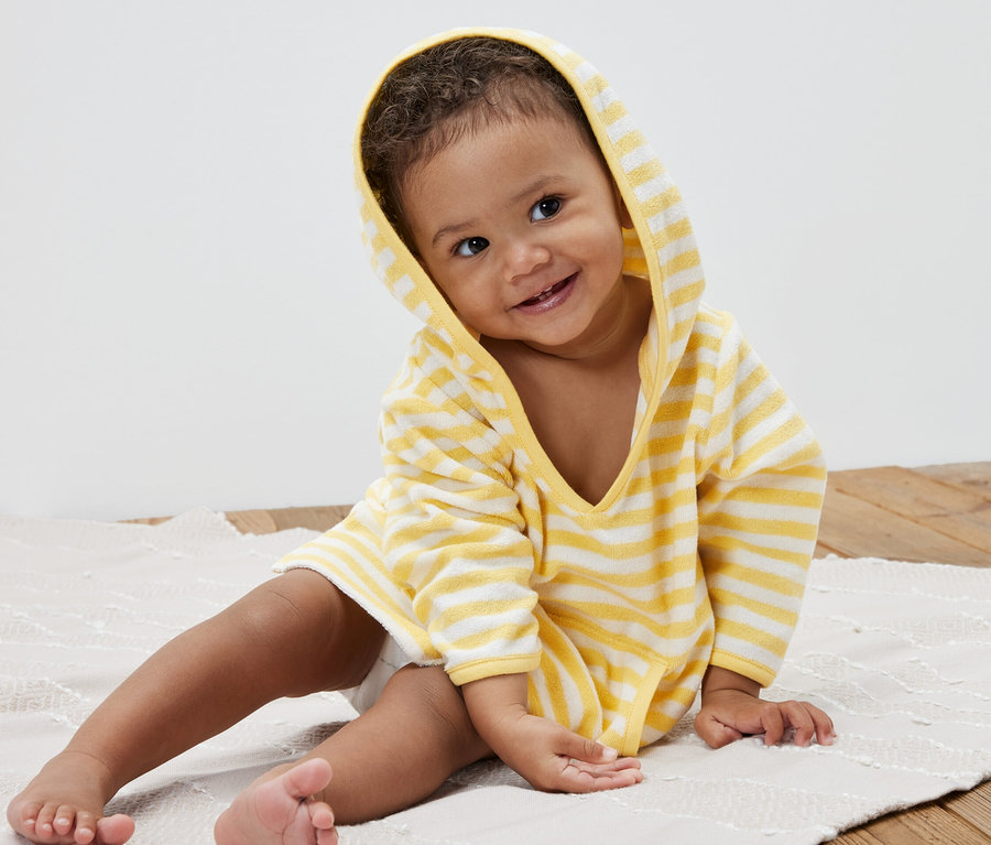 Ein lächelndes Kind sitzt auf einer Unterlage und trägt einen gestreiften Kinder-Frottierponcho.