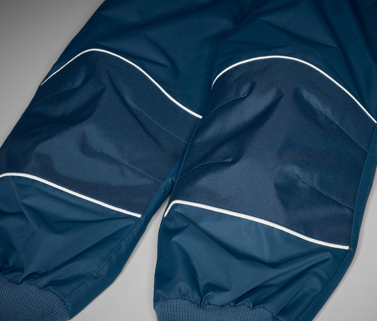 Detailaufnahme einer Kinder-Regenhose mit Mitwachsfunktion und Reflektoren.