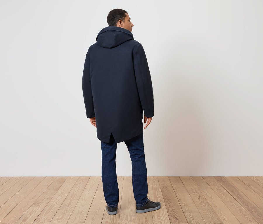 Mann von hinten, trägt einen dunkelblauen Mantel mit Kapuze, Jeans und Schuhe.