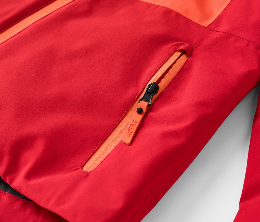 Detailaufnahme einer roten Jacke mit orangefarbenem Reißverschluss und Brusttasche.