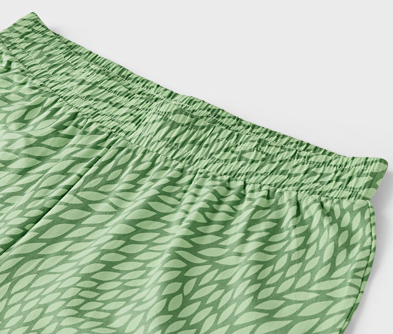 Detail einer grünen Hose mit elastischem Bund und Blattmuster.