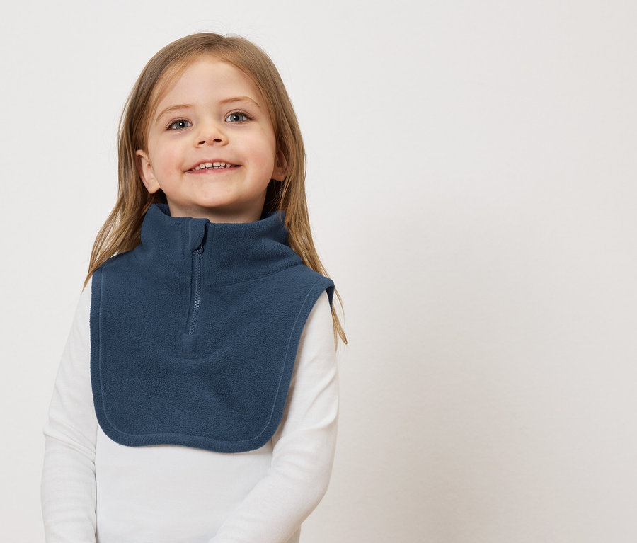 Lächelndes Mädchen mit braunen Haaren und einem blauen Fleece-Kragenwärmer vor einem weißen Hintergrund.