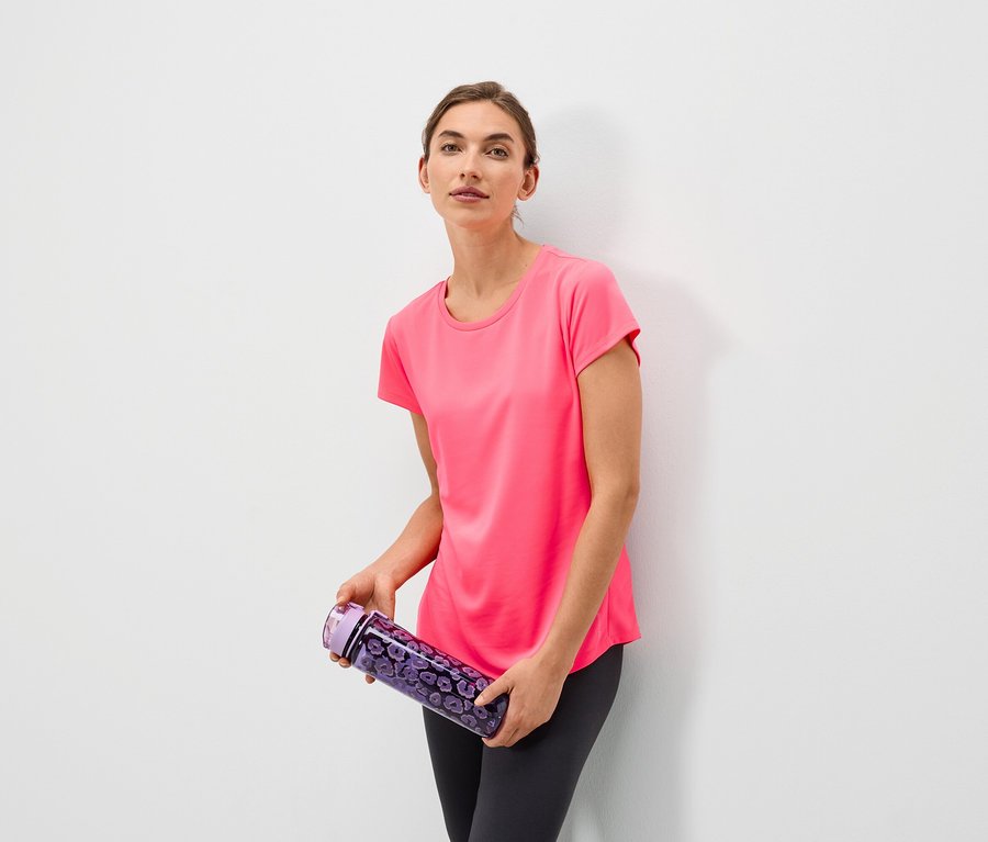 Frau hält eine lila Wasserflasche mit Blumenmuster und trägt ein rosa T-Shirt und graue Leggings.