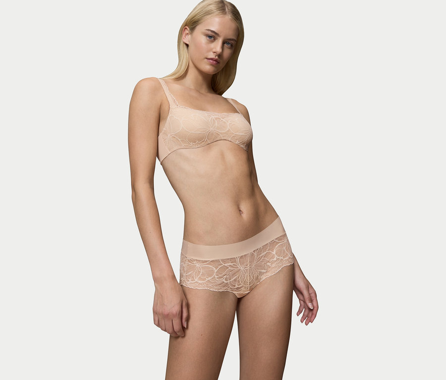 Blonde Frau posiert in einem beigen Spitzen-BH und passenden Slips.
