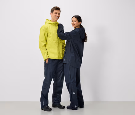 Zwei Personen in Regenjacken und Regenhosen, ein Mann in Gelb und eine Frau in Dunkelblau.