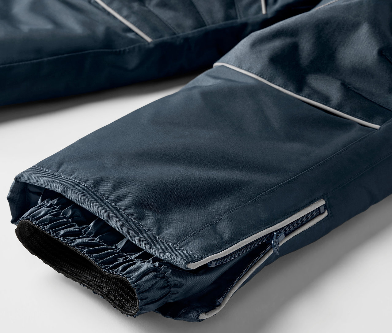 Detailaufnahme der Beinpartie einer marineblauen Skihose mit elastischen Bündchen und Reißverschluss.