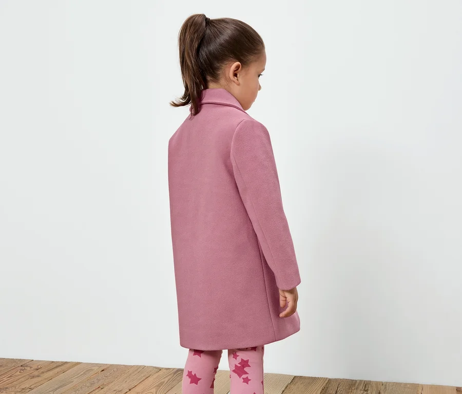 Mädchen in einem rosa Mantel und Leggings mit Sternenmuster, das mit dem Rücken zur Kamera steht.
