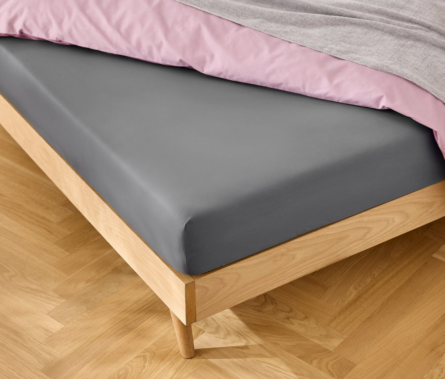 Bett mit grauem Spannbettlaken, rosa Bettwäsche und grauer Decke.