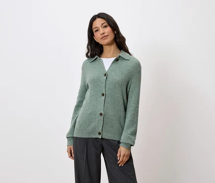 Frau trägt eine grüne Strickjacke mit Knöpfen und graue Hosen.