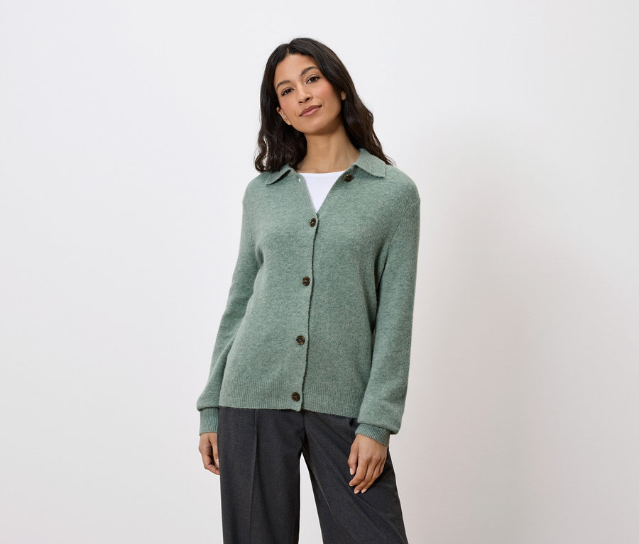 Frau trägt eine grüne Strickjacke mit Knöpfen und graue Hosen.