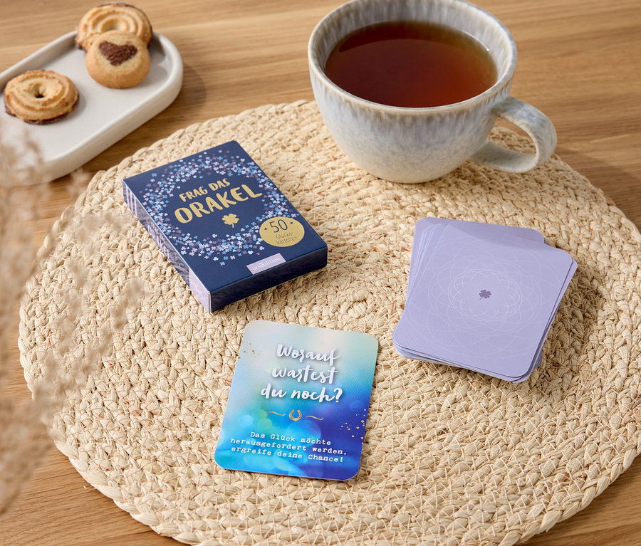 Runder Tischset aus Korbgeflecht mit einer Tasse Tee, Keksen und einem Kartenspiel.