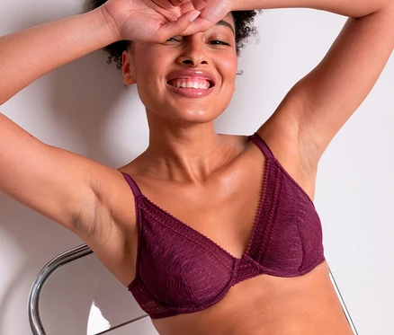 Lächelnde Frau trägt einen dunkelroten Spitzen-Bügel-BH »Leila« von Passionata und passende Slips, lehnt sich mit erhobenen Armen zurück.