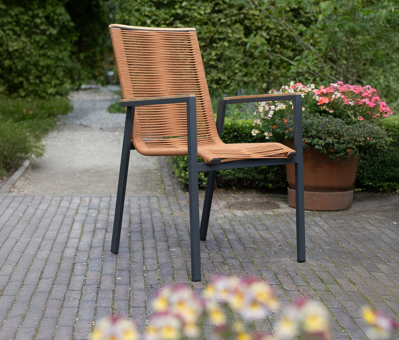 Ein brauner Stuhl mit Armlehnen steht auf einem gepflasterten Weg im Freien.