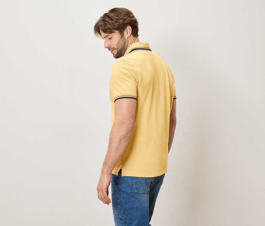 Mann von hinten in einem gelben Poloshirt mit blauen Jeans.