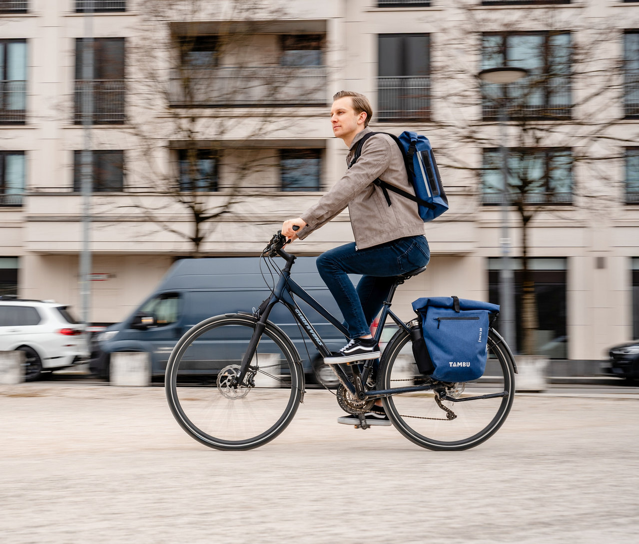 Mann fährt mit Fahrrad mit blauer Tambu »INAYA« Fahrradtasche.