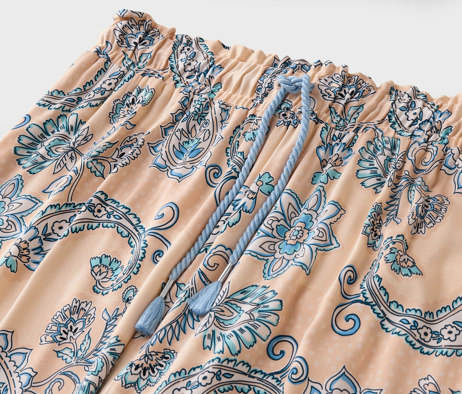 Detailaufnahme einer peachfarbenen Hose mit blauem Blumenmuster und Kordelzug.