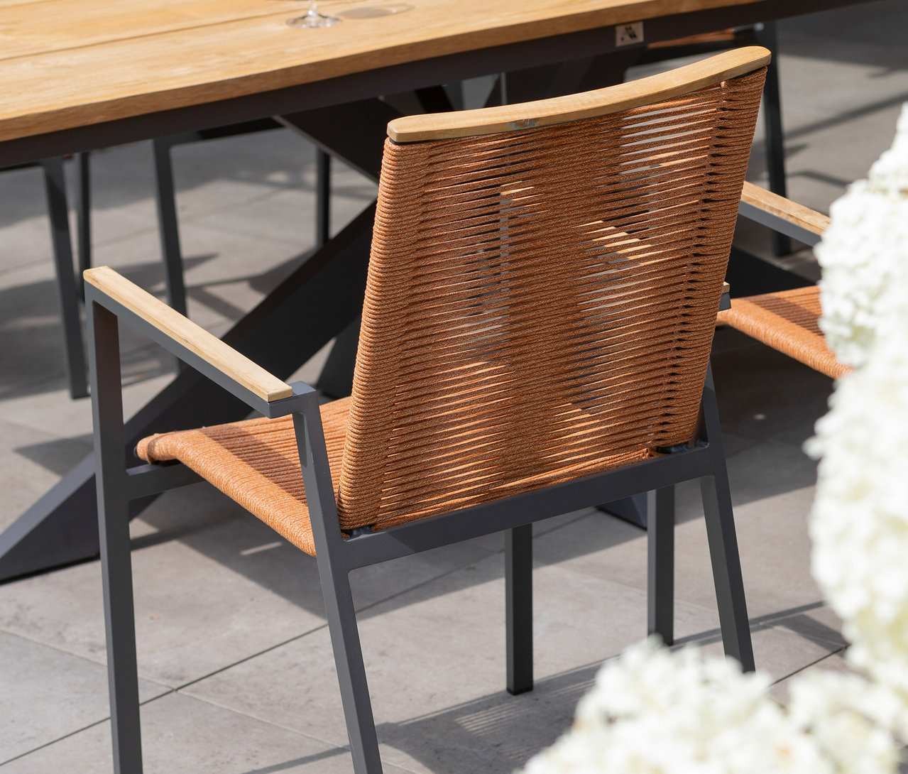 Nahaufnahme von Stühlen mit geflochtenen Rückenlehnen und Armlehnen aus Holz an einem Tisch im Freien.