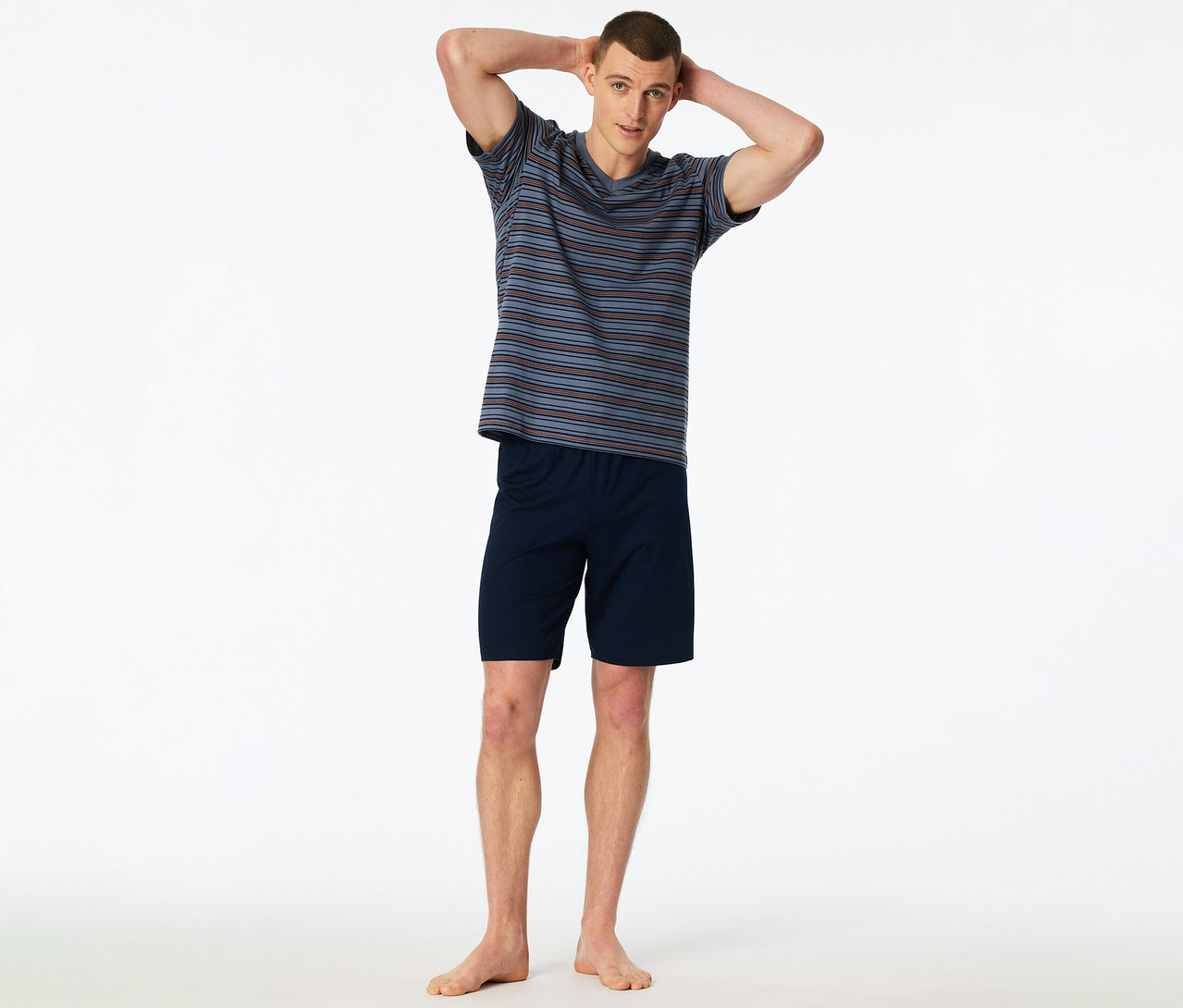 Ein Mann steht mit den Händen hinter dem Kopf und trägt ein gestreiftes SCHIESSER Shorty-Set.
