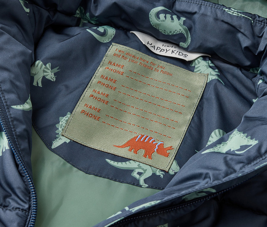 Innenansicht einer blaugrünen Jacke mit Dinosaurier-Muster und einem Etikett mit Platz für Namens- und Telefonnummerangaben.