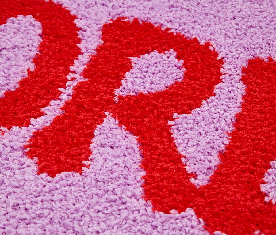 Nahaufnahme eines lilafarbenen Teppichs mit einem roten Buchstaben.