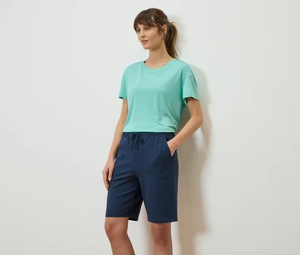 Frau mit Pferdeschwanz, trägt ein türkisfarbenes T-Shirt und marineblaue Shorts.