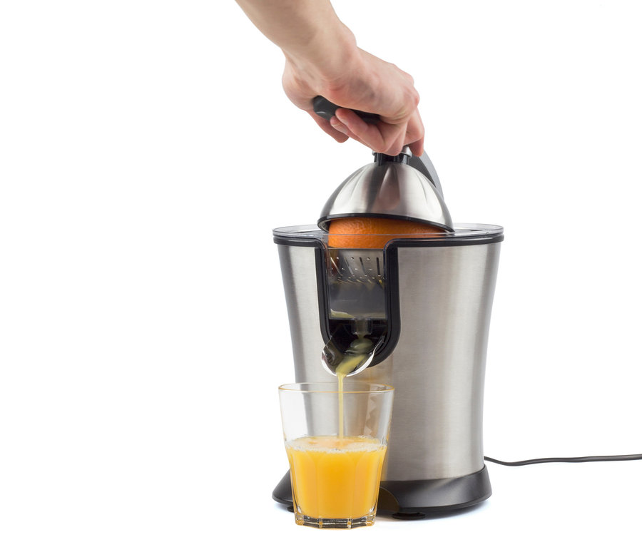Eine Hand presst eine Orange in einer elektrischen Saftpresse aus Edelstahl, wobei der Saft in ein Glas fließt.
