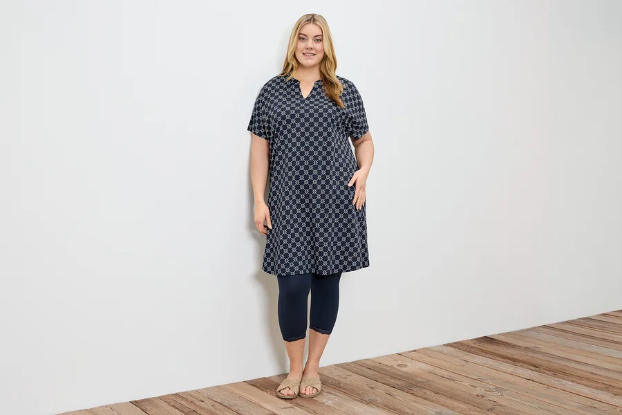 Frau in einem gemusterten Kleid mit dunkelblauen 3/4-Leggings mit Spitzenborte.