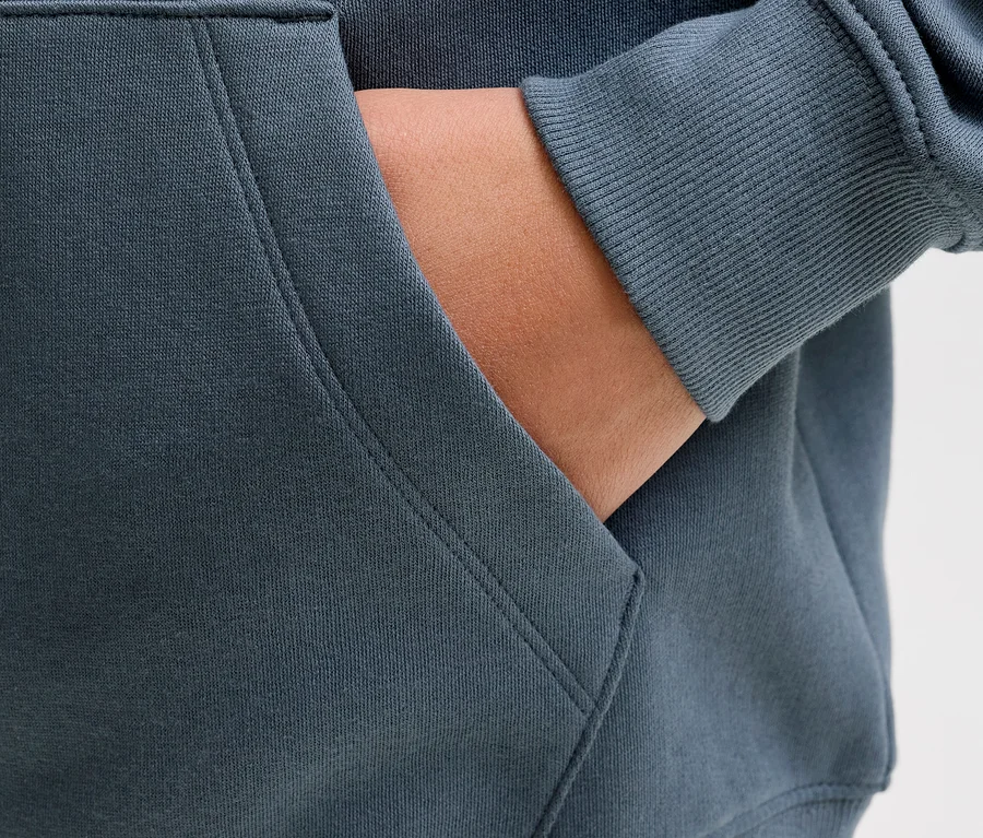 Eine Hand steckt in der Bauchtasche eines dunkelgrauen Jack&Jones Sweat-Hoodies Star.