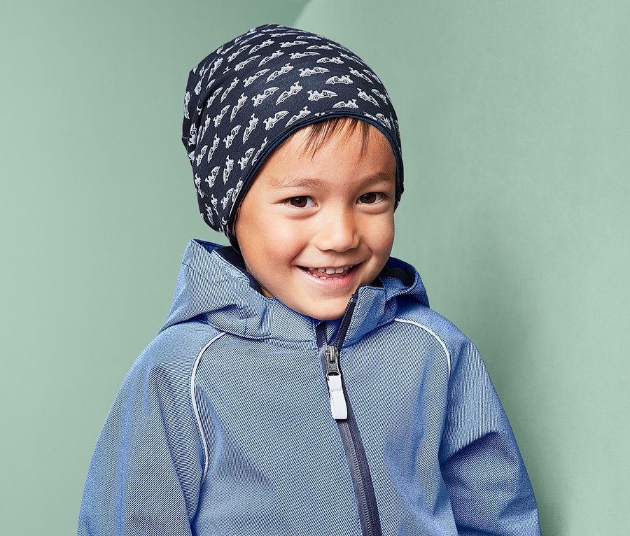 Lächelnder Junge trägt einen blauen Overall und eine Wendemütze.