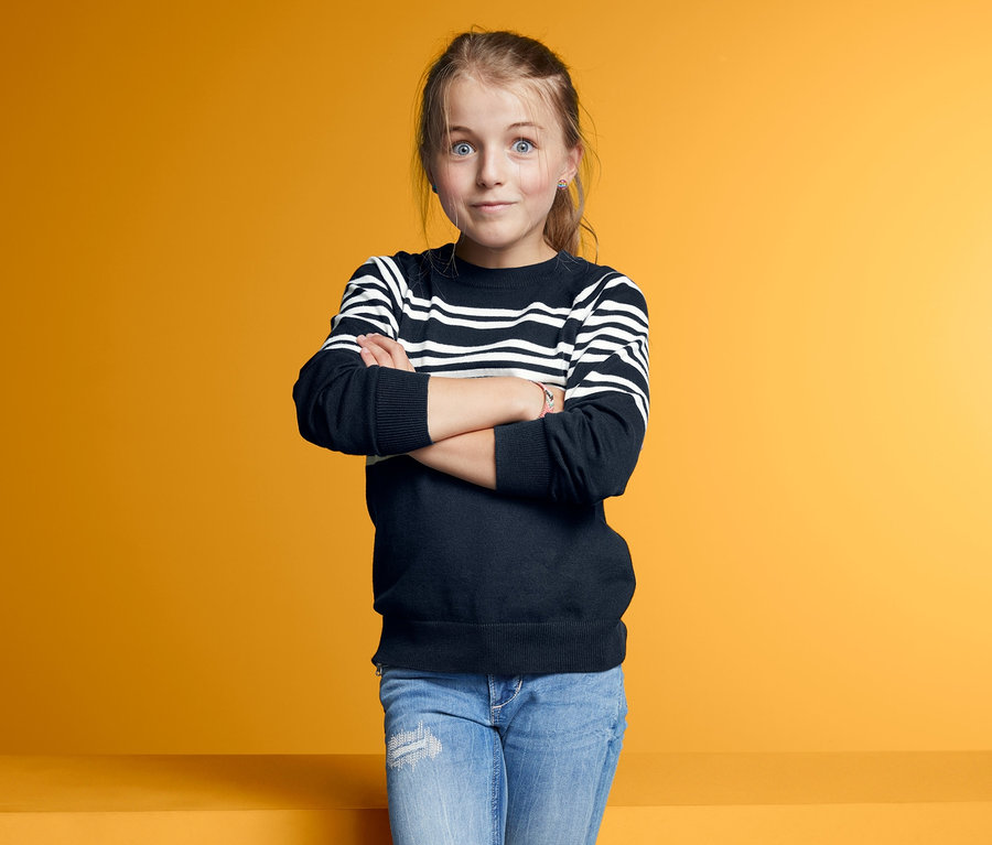 Mädchen posiert mit verschränkten Armen in einem Feinstrickpullover.