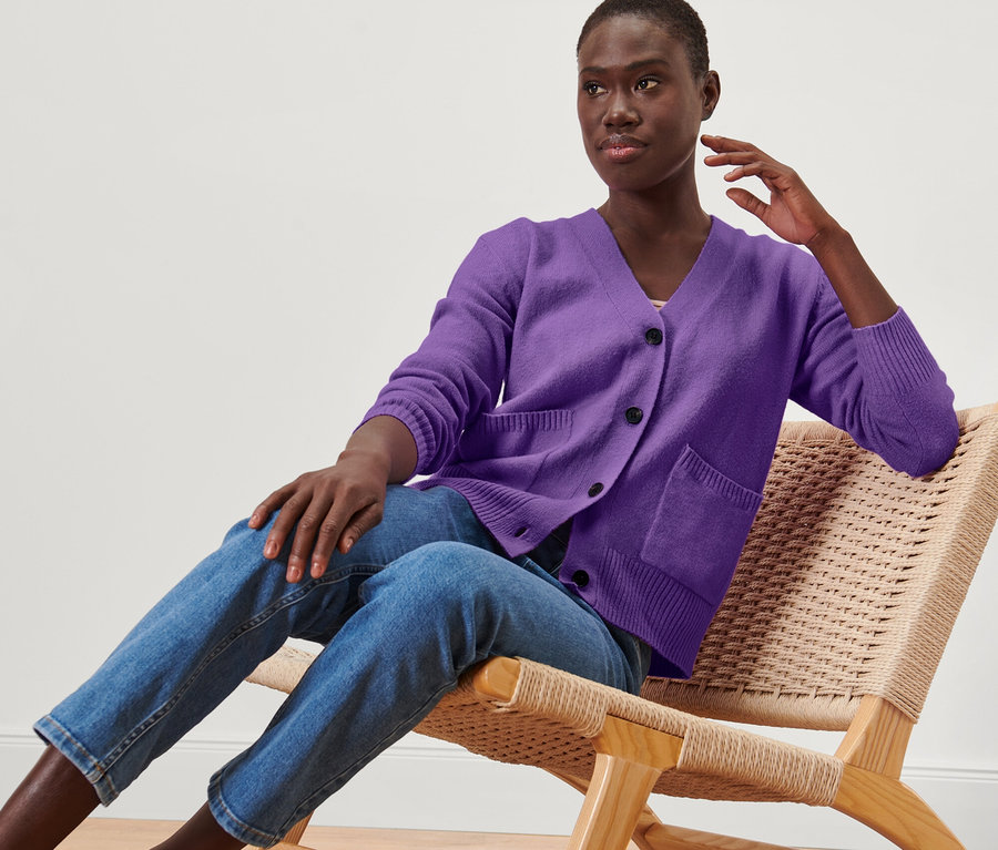 Frau sitzt im Sessel und trägt eine lila Strickjacke mit Wolle.