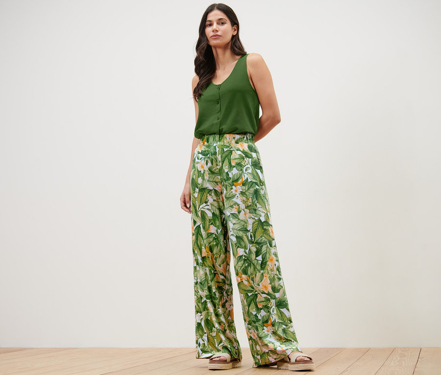 Frau posiert in grünem Top und bedruckter Palazzohose.