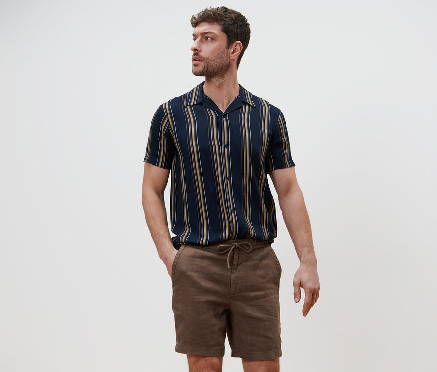 Mann posiert in Leinen-Shorts und gestreiftem Hemd.