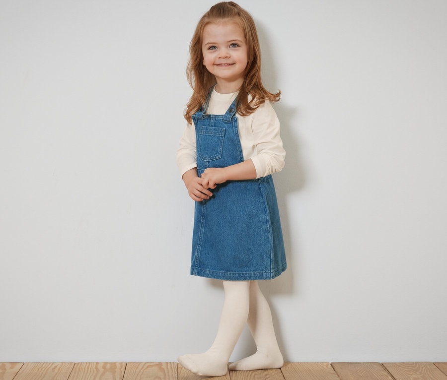 Lächelndes Mädchen posiert im Kinder-Latzkleid.