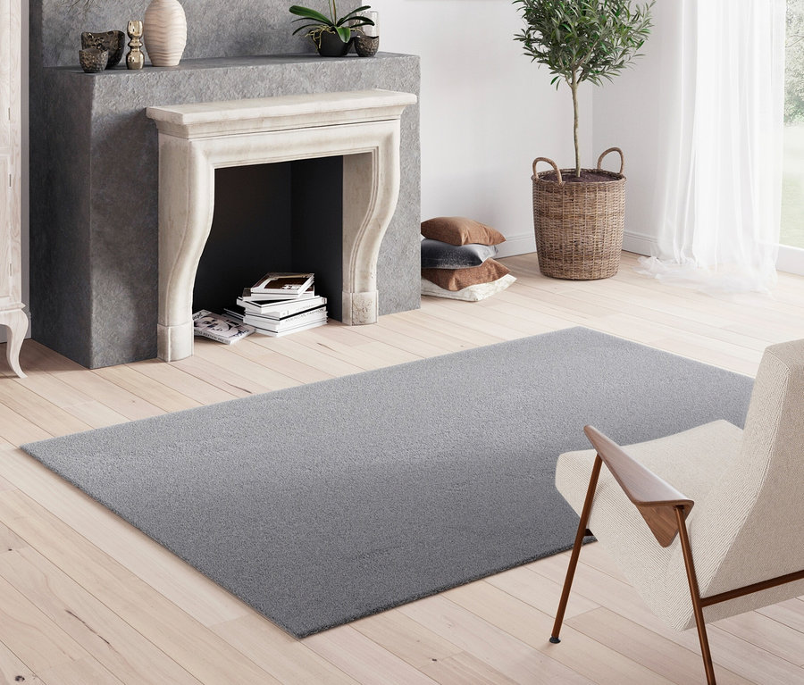Grauer Teppich »Mellow« liegt auf Holzboden im Wohnzimmer mit Kamin.