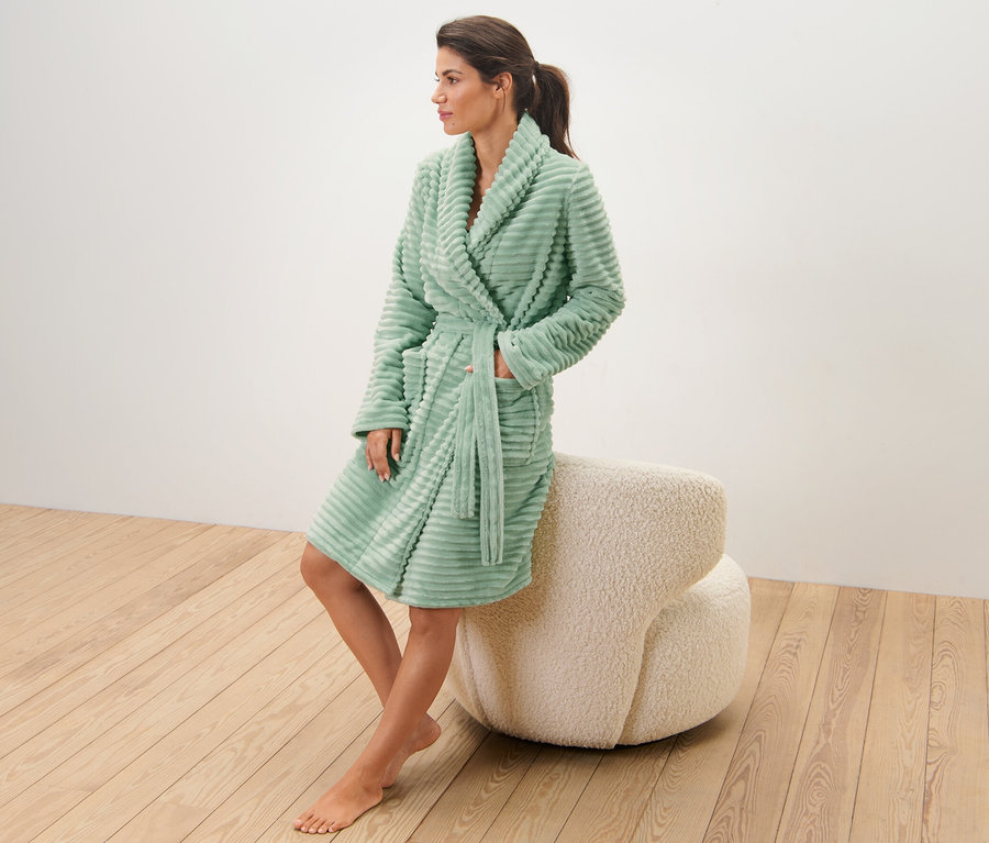 Eine Frau sitzt auf einem dekorativen Hocker und trägt einen Kuschelmantel.