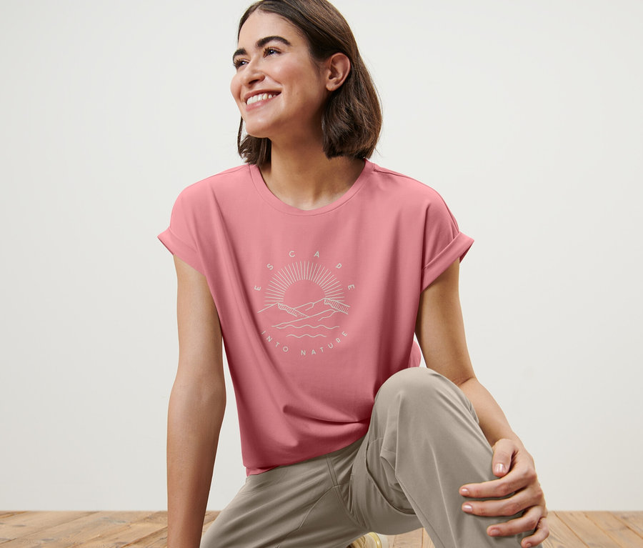 Frau auf Holzboden trägt ein rosafarbenes T-Shirt mit Print.